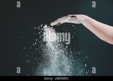 Isoliert auf schwarzem Hintergrund gießt weibliche Hand weißes Mehl wie Schnee zum Backen 2020 Stockfoto