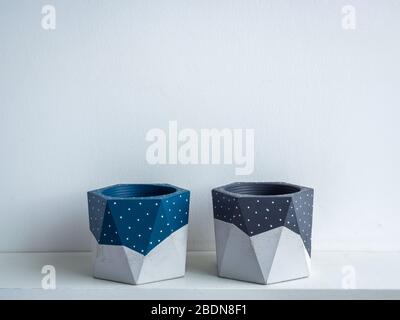 Kaktustopf. Betontopf. Leere blau und grau bemalte moderne geometrische Beton Pflanzgefäße auf weißem Holzregal isoliert auf weißem Hintergrund. Stockfoto