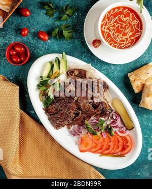 Tomatensuppe und gebratenes Fleisch mit Zwiebeln, Tomaten und Gurken Stockfoto