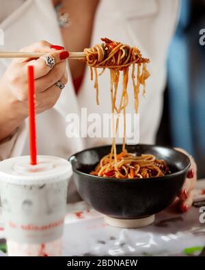 Mädchen hält Hühnernudeln auf Sushi-Sticks Stockfoto