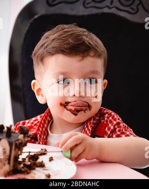 Kleiner Junge isst Kuchen und wird schmutzig Stockfoto