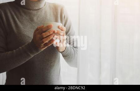 Junge Frau glücklich, am Morgen ausruhen, mit einer Tasse Getränk durch das Fenster schauen.zu Hause bleiben Beratung, um Coronavirus COVID-19 spr Stockfoto