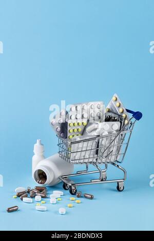 Verschiedene Kapseln, Tabletts und Medikamente im Einkaufswagen und Pillen, die aus der weißen Flasche auf blauem Grund verschüttet werden. Kauf- und Einkaufskonzept für die Medizin. Stockfoto