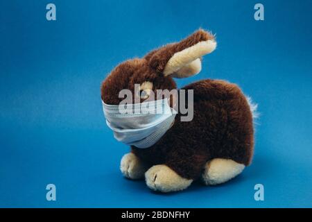 Spielzeughasen stehen in einer medizinischen Maske auf blauem Hintergrund. Konzept des Schutzes vor Atemwegserkrankungen, Viren und individuellen Atemschutzmaßnahmen. Coronavirus stoppen. Stockfoto
