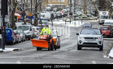 Winterschnee in der Stadt (verkehrsreiche Straße, Autos geparkt, Kompakttraktor wartet an der Ampel im Stadtzentrum) - Brook Street, Ilkley, Yorkshire, England, Großbritannien. Stockfoto