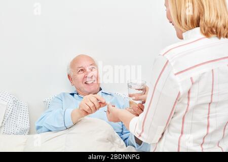Weibliche Pflegeassistentin gibt Oberin der Bettmedizin und ein Glas Wasser Stockfoto