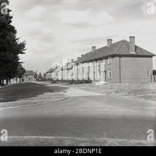 1950er Jahre, historische, Außenansicht der neu gebauten ländlichen Wohnanlage nach dem Krieg, bestehend aus zweistöckigen gemauerten Doppelhaushälften für lokale Arbeiter, Bedford, England, Großbritannien. Während ein Grundentwurf aus architektonischer Sicht, ökologisch gab es Platz für Bäume und offene breite Fußwege zu Fuß auf und so ein gesunder Ort zum Leben. Stockfoto