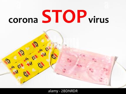 Zwei Kinder rosa und gelbe medizinische Maske auf weißem Hintergrund mit Worten STOPPEN Coronavirus. Masken - Mittel zum persönlichen Schutz gegen Viren. Pandemie Stockfoto