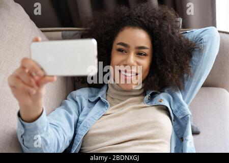 Entspannte afrikanische Frau halten Smartphone Film ansehen, Videoanruf zu Hause. Stockfoto