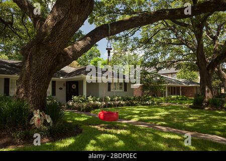 Horizontale Ansicht einer roten Reifenschaukel, die von einem Baum in einem exklusiven freistehenden Wohnhausgarten, West Alabama St, Afton Oaks, Houston, Texas hängt Stockfoto