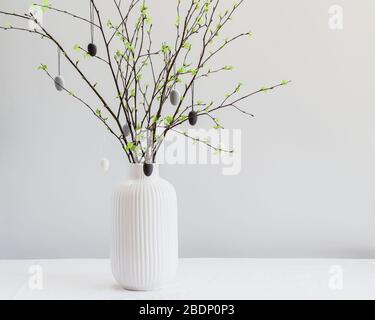 Osterbaum auf einem weißen Tisch. Birkenzweige mit weißen und grauen bemalten Eiern. Postkarte mit einem Kopierbereich Stockfoto