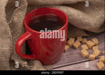 Ein roter Keramikbecher mit Tee und Brocken von braunem Rohrzucker. Nahaufnahme Stockfoto