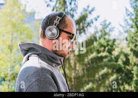 Bärtiger Mann im Hoodie mit Kopfhörern, die Musik im Park im Freien, Kopf und Schultern hören Stockfoto