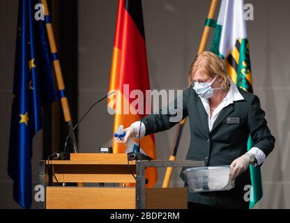 09. April 2020, Sachsen, Dresden: Eine Usherfrau reinigt nach der Rede des Parteichefs der AfD-Bundestagsfraktion in Sachsen während einer Sondersitzung des Sächsischen Landtags im IStGH (Internationales Kongresszentrum) den Rednerpult. der Landtag tagelang erstmals seit 1993 nicht mehr in seinem offiziellen Plenarsaal. Auf der Tagesordnung stehen unter anderem die Erklärung einer "außerordentlichen Notsituation" nach Artikel 95 der Landesverfassung Sachsen und die Diskussion über die Gesetzesentwürfe der Landesregierung zur Einrichtung eines Sonderfonds "Stabilisierungsfonds" Stockfoto
