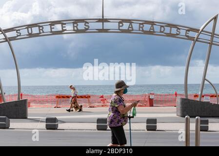 Eine Frau geht an einem Surfers Paradise Zeichen vorbei, während sie eine Schutzmaske als präventive Maßnahme gegen die Verbreitung von Coronavirus trägt.Council hat einen außergewöhnlichen Schritt unternommen, einige Goldküstenstrände als präventive Maßnahme gegen die Ausbreitung von Coronavirus zu schließen, nachdem Tausende von Menschen soziale Distanzierungsregeln ignorierten. Strände am Spit, Surfers Paradise und Coolangatta werden ab Mitternacht geschlossen. Der Rest der Strände der Stadt bleibt für die Leute offen, um zu trainieren, zu schwimmen oder zu surfen, aber der Rat sagt, dass es nicht zögern wird, mehr Strände zu schließen, wenn die Leute weiterhin die Regeln durchziehen. Stockfoto