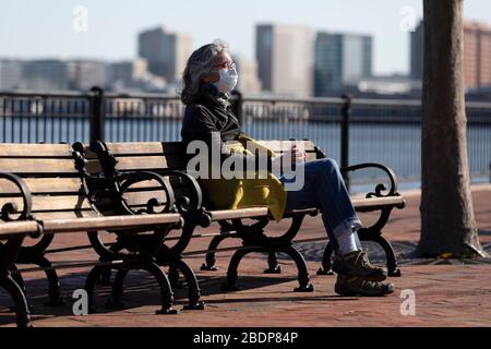 Frau, die eine Gesichtsmaske trägt, während sie auf einer Bank im Piers Park, Boston Massachusetts USA sitzt Stockfoto