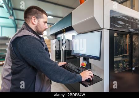 Der Druckereifachmann arbeitet an einem großen modernen 3D-Druckergerät mit Computersteuerung Stockfoto