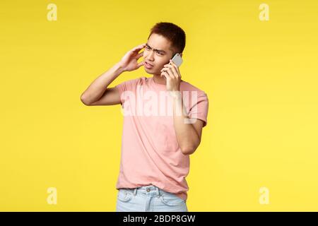 Technologie-, Kommunikations- und Lifestyle-Konzept. Unzufriedenen asiaten in pinkfarbenem T-Shirt, frustriert, mit Handy telefonieren, quietscheln und grimacken Stockfoto