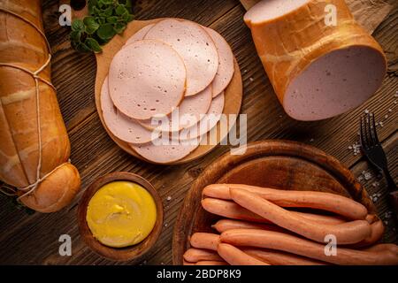 Zusammensetzung von Feinkost und Wiener Würstchen mit Senf auf Holzschneidebrett serviert, flach legen Stockfoto