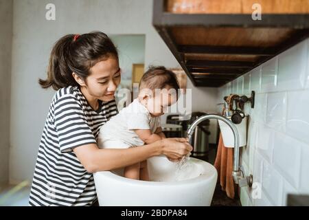Mutter helfen ihrem Baby, die Hand in der Spüle zu waschen Stockfoto