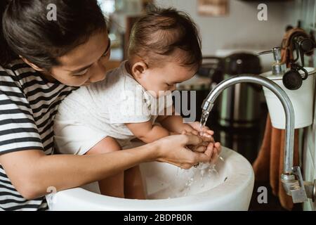 Mutter helfen ihrem Baby, die Hand in der Spüle zu waschen Stockfoto
