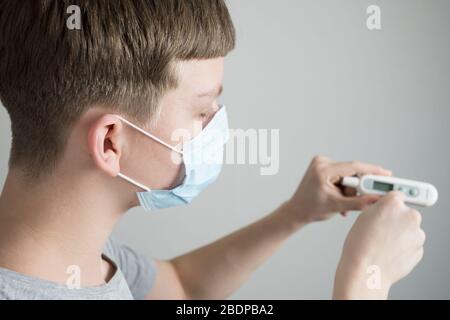 Teenager in medizinischer Maske hält Thermometer in den Händen und misst Temperatur. Covid 19. Isoliert. Nahaufnahme. Prävention von Coronavirus. Stockfoto