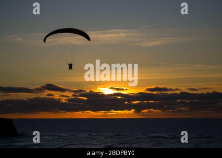 Silhouette eines Paragleiters, der bei bewölktem Sonnenuntergang über dem Meer fliegt. Sportkonzept Gleitschirmfliegen Stockfoto