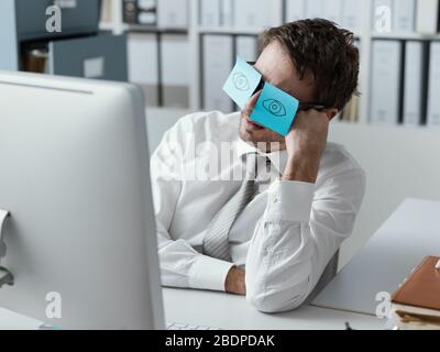 Fauler unproduktiver Büroangestellter, der lustige Haftnotizen auf seiner Brille trägt und seine geschlossenen Augen versteckt Stockfoto