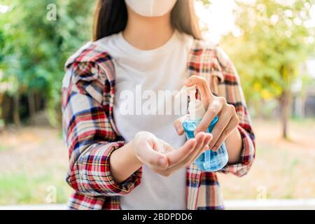 Junge Frau, die mit einem antiseptischen Alkoholhandgel ihre Hände, verschwommene Bäume und Gartenhintergrund säubert, gutes Hygienekonzept Stockfoto