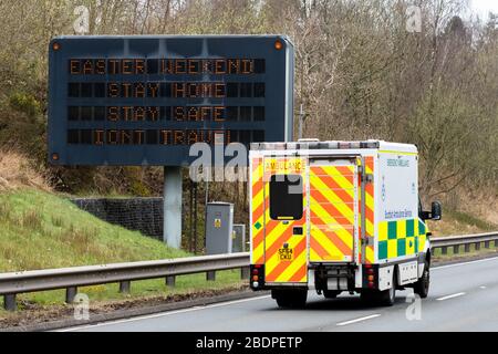 A82 von Loch Lomond, Schottland, Großbritannien. April 2020. Reisesorgen am Osterwochenende - ein Krankenwagen passiert ein Schild, in dem die Menschen aufgefordert werden, zu Hause zu bleiben und nicht über das osterwochenende auf der A82 nordwärts an der Seite von Loch Lomond Credit zu reisen: Kay Roxby/Alamy Live News Stockfoto