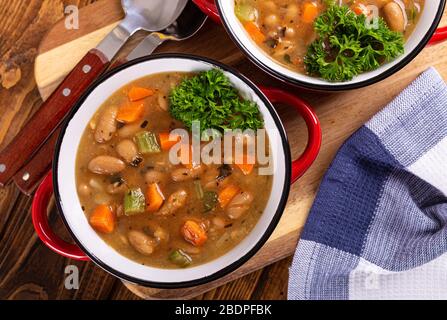 Blick von oben auf leckere Bohnensuppe mit Karotten und Sellerie in einer Schüssel auf einem Holztisch Stockfoto