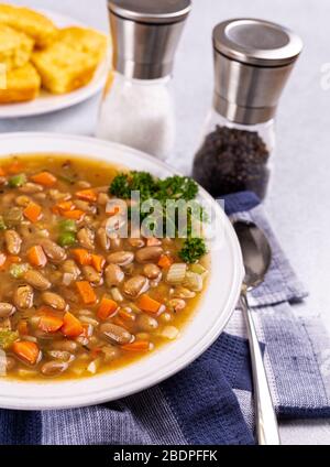 Bohnensuppe mit Karotten und Sellerie in einer weißen Schüssel mit Maisbrot im Hintergrund Stockfoto