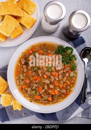 Ansicht von oben auf die Bohnensuppe mit Karotten und Sellerie in einer weißen Schüssel mit Maisbrot im Hintergrund Stockfoto