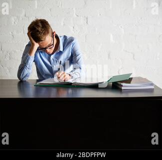 Aufnahme eines jungen Mannes, der während seiner Arbeit an seinem Büroschreibtisch einige Papiere überprüft Stockfoto