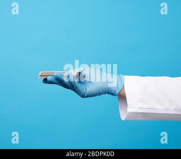 Arzthand in blauen medizinischen Latexhandschuhen hält eine leere Visitenkarte auf blauem Grund, Platz für eine Beschriftung Stockfoto
