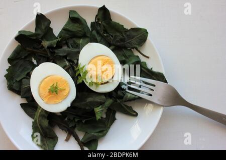 Frühlingssalat mit frischem Löwenzahn und hart gekochten Eiern in weißem Teller auf weißem Holzhintergrund. Nahaufnahme, Draufsicht, Kopierbereich Stockfoto