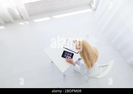 Kaukasische Ärztin mit Tablette und Schreiben Diagnose in medizinischen Formen Dokumente. Draufsicht Stockfoto