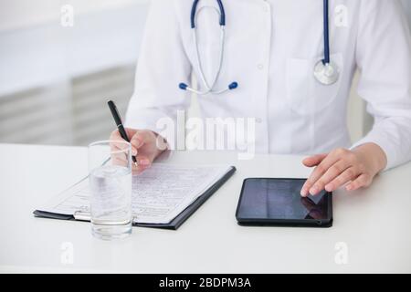 Kaukasische Ärztin mit Tablette und schriftlich Diagnose in medizinischer Form und Dokumente. Nahaufnahme Stockfoto