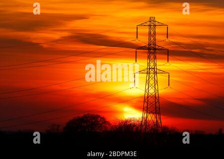 Ein Strommast, der gegen die untergehende Sonne in Shillington, Leeds, Großbritannien, schillert Stockfoto
