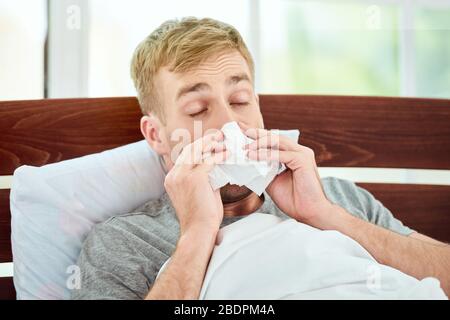 Portrait eines kranken jungen Mannes mit runniger Nase, der an Kälte oder Grippe leidet und während er zu Hause im Bett liegt. Viruserkrankung. Coronavirus Konzept. Konzept für das Gesundheitswesen Stockfoto
