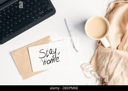 Bleiben Sie zu Hause während Coronavirus COVID-19 Quarantäne, Selbstisolierung, Sperrkonzept. Femininer Arbeitsbereich mit Top View, Laptop, Kaffeetasse, Decke und lett Stockfoto