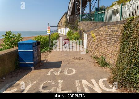 Southend-on-Sea, Großbritannien. April 2020. Eine asphaltierte Fußgängerroute entlang der Küste von Southend ist vorübergehend für Fußgänger gesperrt, da sie während der COVID-19-Pandemie wegen sozialer Distanz eingeschränkt ist. Auf dem Boden ist ein gut sichtbares Schild mit dem Hinweis „KEIN RADFAHREN“ angebracht und auf roten Warnschildern angebracht. Der Weg verläuft am Strand entlang und wird von einer Ziegelmauer und einer Betonbarriere mit einer Metallkonstruktion über dem Kopf begrenzt. Die Maßnahmen spiegeln die Bemühungen der öffentlichen Gesundheit wider, die Überlastung zu verringern und sichere Distanz zu wahren. Penelope Barritt/Alamy Live News Stockfoto