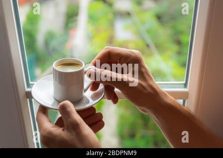 Mann Hände halten kleine Tasse Kaffee in der Nähe Fenster in Morgensonne Stockfoto