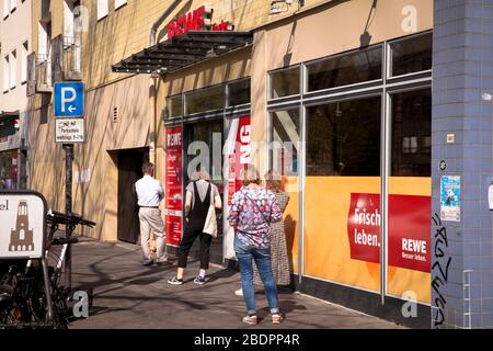 Coronavirus/Covid 19-Ausbruch, 8. April. 2020. Menschen, die in einer Warteschlange vor einem REWE-Supermarkt an der Neusser Straße, Köln, stehen. Coro Stockfoto