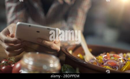 Frau sucht auf ihrem digitalen Tablett nach gesunden Rezepten und kocht frisches gemischtes Gemüse in einem Tontopf Stockfoto