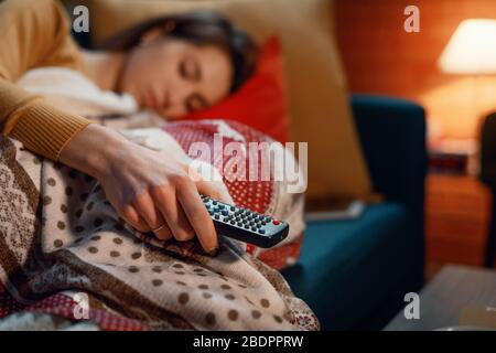 Frau, die zu Hause auf dem Sofa einschläft, während sie Fernsehen, hält sie die Fernbedienung Stockfoto