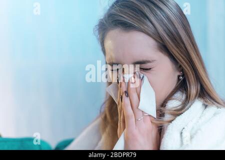 Junge Frau, die sich mit einer Decke bedeckt und ihre Nase weht, hat Kälte und Grippe Stockfoto