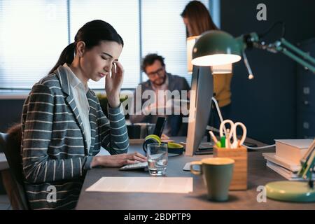 Junge, professionelle Geschäftsfrau, die am Schreibtisch sitzt und arbeitet, hat Kopfschmerzen und fühlt sich gestresst Stockfoto