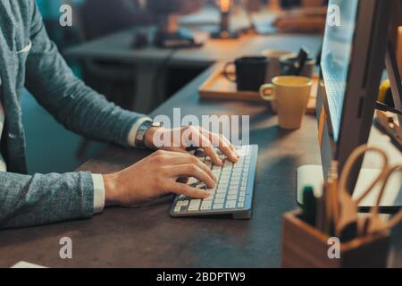 Der im Büro arbeitende Unternehmer sitzt am Schreibtisch und tippt auf die Computertastatur, das Geschäfts- und Technologiekonzept Stockfoto