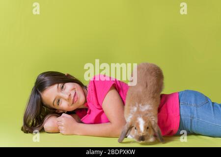 Kleines Mädchen spielt mit ihrem Haustier Kaninchen auf dem Boden liegend mit dem Kaninchen läuft auf dem Rücken, in einem Studio, mit lebendigen Farben. Selektiver Fokus auf t Stockfoto